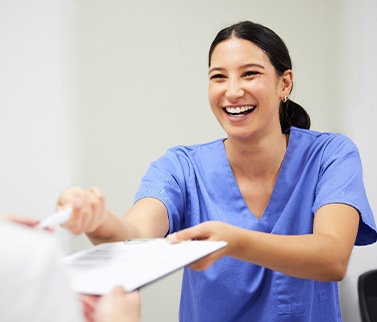 Dental assistant smiling while handing patient form