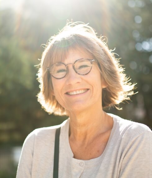 Woman with glasses smiling outdoors after replacing missing teeth in Worcester