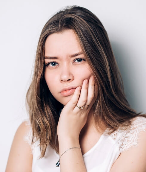 Young woman holding her cheek in pain before wisdom tooth extractions in Worcester